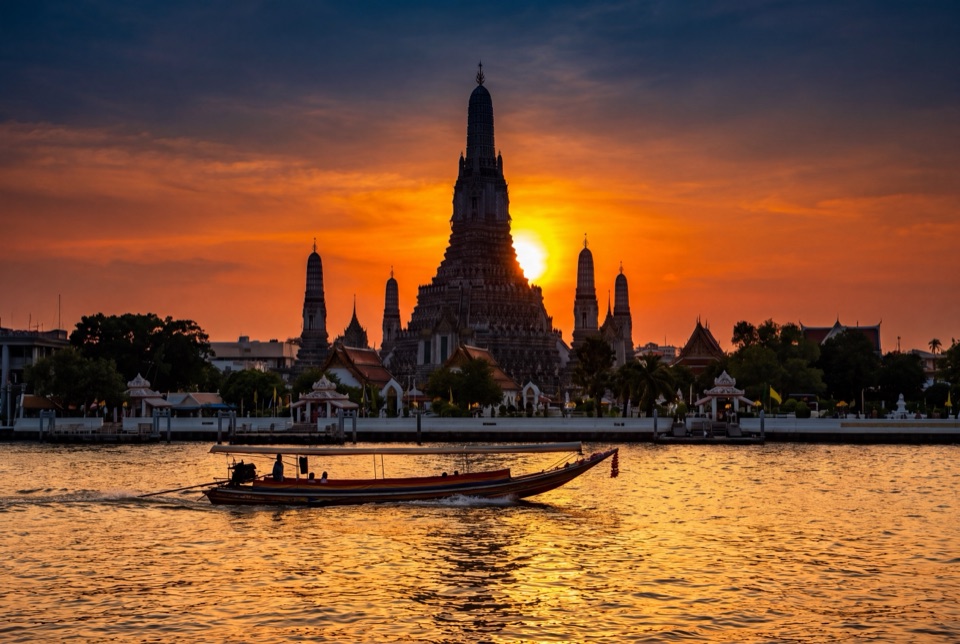 Gün batımında Chao Phraya Nehri kıyısında Wat Arun ve nehirde ahşap tekne